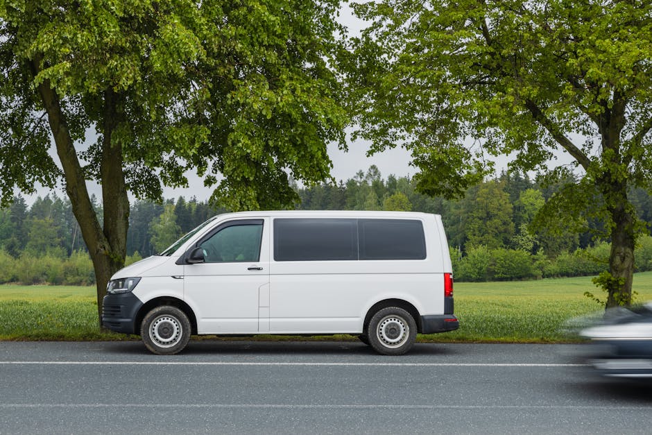 A white moving van parked outside a residential building with a brick facade, displaying the company name 'Man with Van Merton Park' and the service category 'removals' on its side. The side door of t
